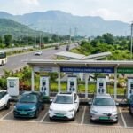 एक एक्सप्रेसवे के पास स्थित टाटा पावर ईजेड चार्जिंग स्टेशन (Tata Power EZ Charge station) का विस्तृत लैंडस्केप दृश्य, जहां पांच इलेक्ट्रिक कारें चार्ज हो रही हैं।