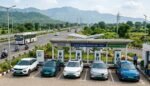 एक एक्सप्रेसवे के पास स्थित टाटा पावर ईजेड चार्जिंग स्टेशन (Tata Power EZ Charge station) का विस्तृत लैंडस्केप दृश्य, जहां पांच इलेक्ट्रिक कारें चार्ज हो रही हैं।