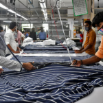 गर्मी से प्रभावित टेक्सटाइल फैक्ट्री का दृश्य, जहां श्रमिक उच्च तापमान में मशीनों के बीच काम कर रहे हैं, हीट स्ट्रेस के कारण घटती उत्पादकता को दर्शाता हुआ।