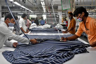 गर्मी से प्रभावित टेक्सटाइल फैक्ट्री का दृश्य, जहां श्रमिक उच्च तापमान में मशीनों के बीच काम कर रहे हैं, हीट स्ट्रेस के कारण घटती उत्पादकता को दर्शाता हुआ।