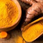 Wooden bowls filled with turmeric powder and fresh turmeric roots