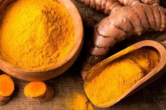 Wooden bowls filled with turmeric powder and fresh turmeric roots