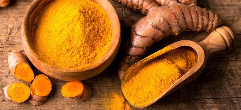 Wooden bowls filled with turmeric powder and fresh turmeric roots